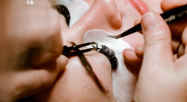 A person having their lashes meticulously placed using two tweezers.